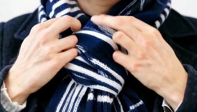 Close-up of person tying a striped scarf around their neck.