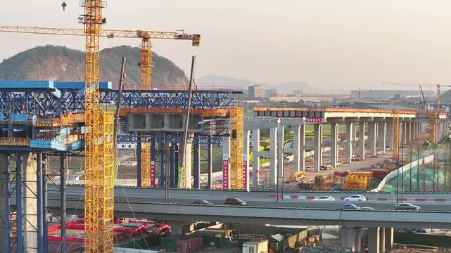 Urban elevated highway construction site with multiple cranes and busy activity during dusk