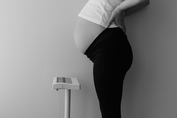 Black and white photo of pregnant brunette woman standing on scale during pregnancy weight control showing maternal health body changes medical monitoring and mindful prenatal care concept