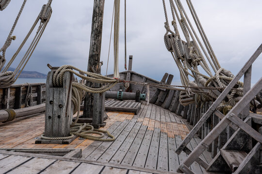 Wide Angle View of the Wooden Deck of an Ancient Sailing Ship Bow, Showing the Windlass Mechanism and Grate with Coastal Landscape in the Background.