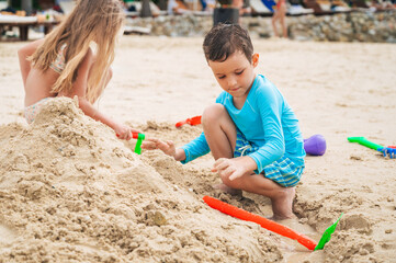 Cute child boy plays on beach and builds a sand castle with friends in summer by the sea on vacation