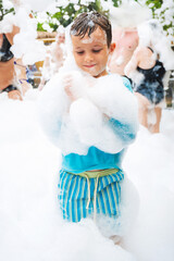 Happy white child boy smiles at a foam party on the beach in summer on vacation