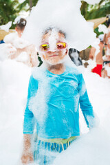 Happy child boy at a foam party on the beach in summer on vacation