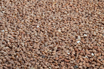 Industrial bulk buckwheat pattern, Granular buckwheat surface with shadows and husk pieces, Closeup of densely packed buckwheat kernels showing depth and husk fragments