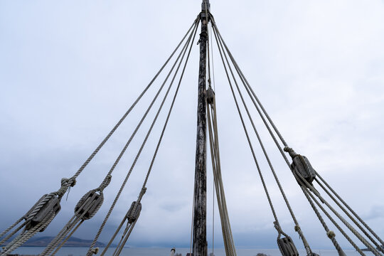 Low Angle View of Ship Mast and Intricate Rigging Ropes and Pulleys Against a Bright Overcast Sky, Emphasizing Nautical Structure and Tension.
