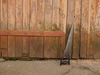 Hand saw leaning against old wooden doors with rust and time marks, workshop or yard scene.
