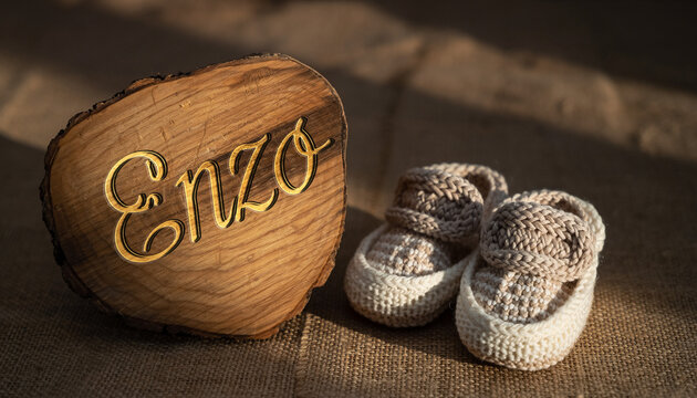 Baby name Enzo engraved on a wooden plaque with knitted baby shoes. Image for baby name reveal