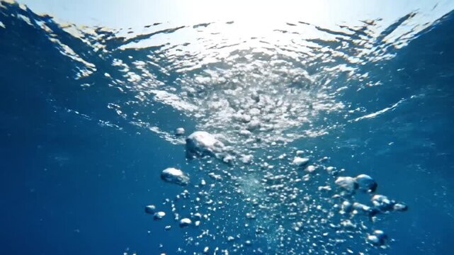 A vibrant underwater perspective reveals a mesmerizing cascade of clear bubbles gracefully ascending through deep blue water. Sunlight filters from the surface, illuminating the dynamic movement of th