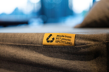 "PET Plastic upcycling" product label tag on the sofa seat fabric material part. Sign and symbol object photo, selective focus.