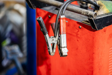 Close up, detail image of red and black insulated jumper cables with metal alligator clips used to charge or jump start a dead car battery.