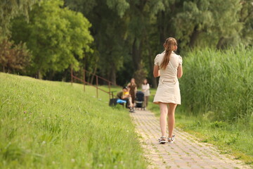 A young girl in a revealing outfit with bare legs walks along a park alley among the greenery to meet her friends. Fashion of modern youth.