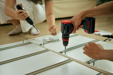 Closeup couple is working with furniture assembly using electric screwdriver