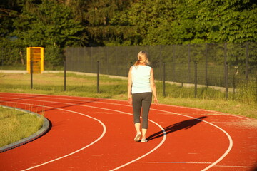 A woman runs on the treadmill of a stadium around a football field. Artificial cover of the sports complex. Activity for weight loss and a healthy lifestyle. Preparing for the competition. Free time