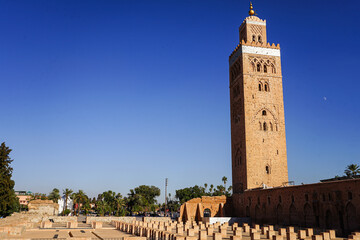 Fototapeta premium Koutoubia-Moschee in Marrakesch: Das markante Minarett aus rötlichem Sandstein erhebt sich vor tiefblauem Himmel über die historische Altstadt. 
