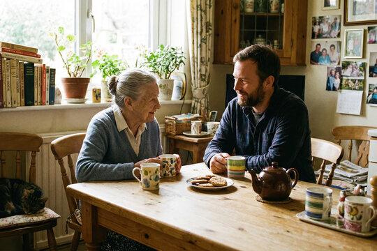 Warm family visit at a cozy kitchen table, elderly woman and adult man sharing tea and cookies, intergenerational conversation and care, generative AI