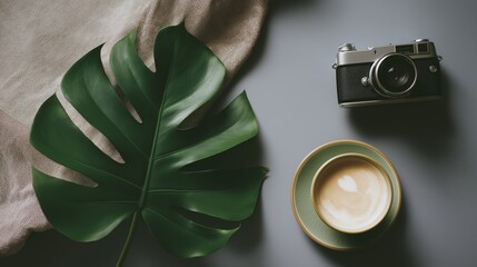 Artful arrangement featuring a monstera leaf a coffee cup with a latte and a vintage camera on the right side against a grey background.