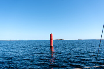 Red navigation buoy stands tall in the calm blue sea under a clear sky