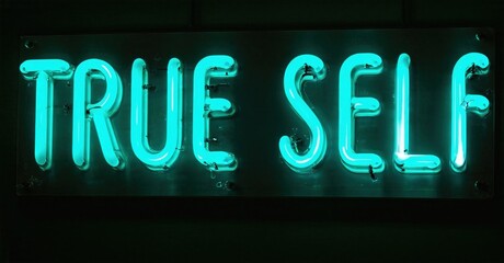 Fototapeta premium Bright turquoise neon sign displays words True Self against dark background. Simple, bold lettering creates striking visual impact.
