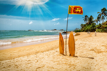 Two surfboards are standing in sand on the beach by the ocean with Sri Lanka flag