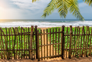 Wooden fence with entrance to the tropical beach at sunset
