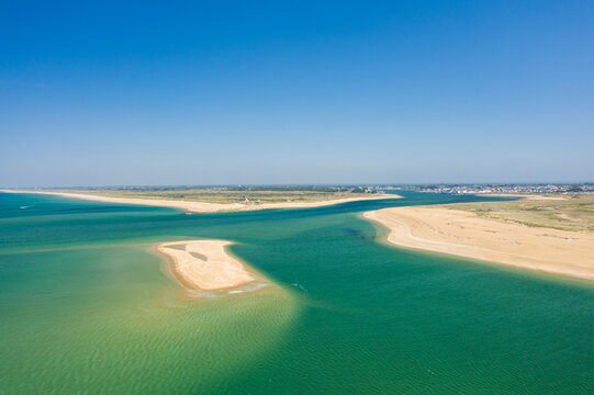 Expansive aerial panorama of the Barre d'Etel sandbank with turquoise water and golden sandy shores under a clear blue sky. The tranquil coastal scene features vivid colors and sweeping natural forms.
