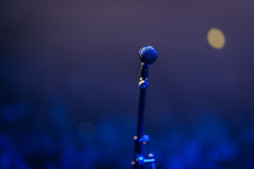 Microphone on a stand illuminated by blue stage lights, creating a vibrant atmosphere for a live...