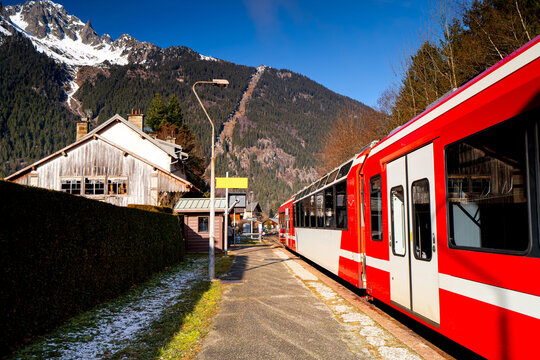Red train stands at Les Praz de Chamonix train station overlooking the mountains. French railway in the Alps with ski resorts.