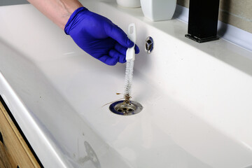 Cleaning  drain hole of bathroom sink with brush, close-up of gloved hand, clearing a blockage © Alsu