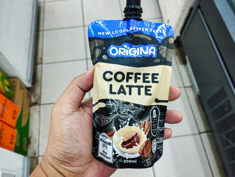 A hand holding a 200ml pouch of Origina Coffee Latte, a ready-to-drink caffeine beverage with a convenient spout.
