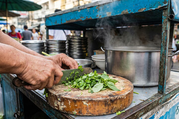 Street food vendor chopping fresh herbs at a busy market stall, hands-on cooking process and everyday local cuisine preparation, generative AI
