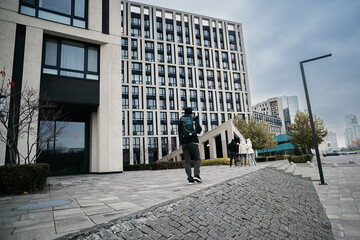 Obraz premium A person with a backpack walks past a striking modern building with a grid facade on a cloudy urban day, capturing contemporary architecture and city life.