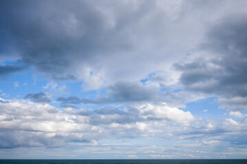 Fototapeta premium Vast cloud-filled sky stretches above a tranquil blue sea, with soft light illuminating the gentle waves near Agde. The scene evokes openness and serenity under shifting weather.