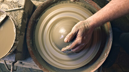 Close-up of a craftsperson's hands shaping clay on a spinning pottery wheel in a workshop, highlighting creativity, craftsmanship, and traditional pottery techniques.