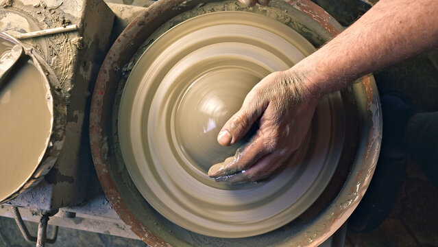 Close-up of a craftsperson's hands shaping clay on a spinning pottery wheel in a workshop, highlighting creativity, craftsmanship, and traditional pottery techniques. - Powered by Adobe