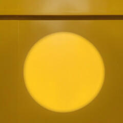 Bright circular light creating a vibrant yellow backdrop on a textured wall during daytime