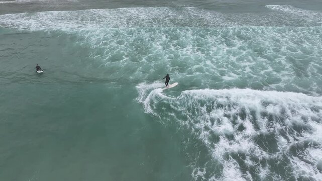 Aerial view of two surfers riding the waves in the ocean, showcasing the contrast between the dark wetsuits and the white foamy water, Bretagne, France.