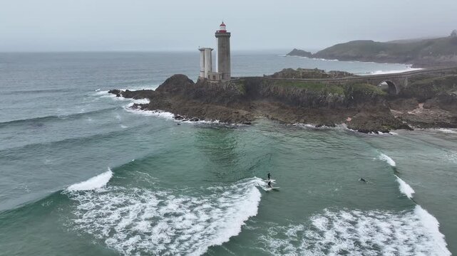 Aerial view of surfers riding waves near the Phare du Petit Minou lighthouse with a bridge in the background, Bretagne, France.