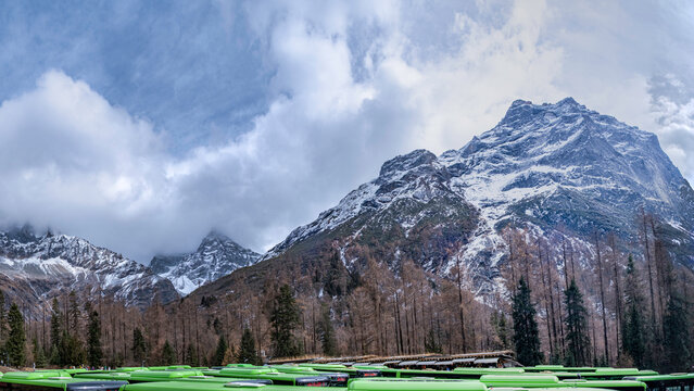 A breathtaking winter mountain landscape covered in deep snow, with dramatic clouds rolling over rugged alpine peaks under a bright blue sky, creating a serene and powerful natural atmosphere.