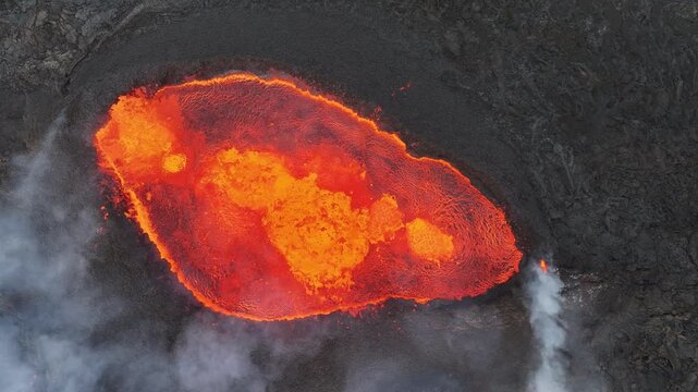 Aerial view of a volcano with fiery orange lava flowing into dark, textured volcanic rock, juxtaposed with plumes of white smoke, Grindavik, Grindavikurbaer, Iceland.