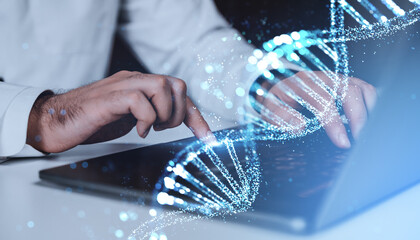 Hands typing on laptop with glowing DNA strand hologram overlay on blue background, symbolizing...