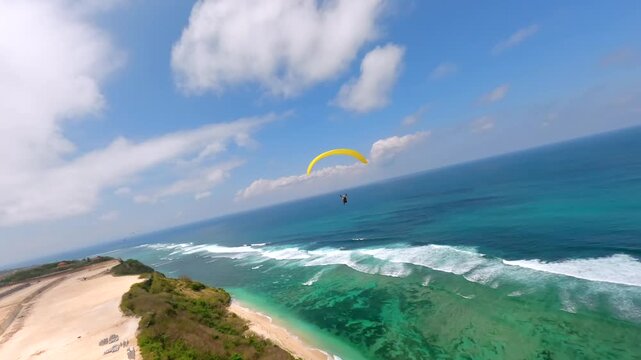 Cinematic FPV drone shot of paragliders gliding over cliffs and turquoise ocean at Pandawa Beach, Bali. Aerial view of scenic coastline, tropical waves, and summer sky.