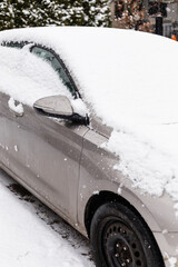 A parked car is covered with a thick layer of snow on a winter evening. Snowflakes fall gently,...