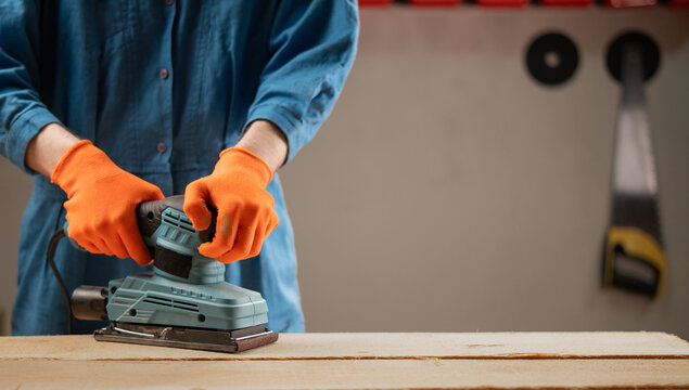 Close up of male hands using a vibration orbital sander to smooth a wooden board surface. Wood finishing process and DIY home improvement concept - Powered by Adobe