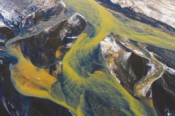 Aerial view of glacial rivers intertwine in a vibrant display of yellow and blue hues, carving through the dark landscape, southern Iceland, Iceland.