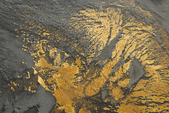 Aerial view of golden rivulets carve through the stark, black volcanic landscape, creating a mesmerizing contrast of color and texture, southern Iceland, Iceland.