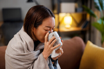 Sick Asian woman drinking hot tea wrapped in blanket at home