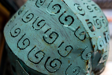 Close-up of a painted turquoise metal surface with raised spiral ornaments and scratches, showing...