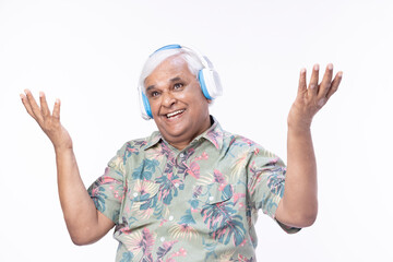 Senior man listening music over headphones and looking up against white background