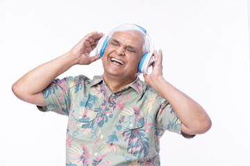 Senior man listening music over headphones and looking up against white background