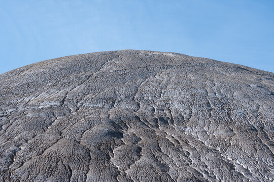 Detailed view of a massive, textured industrial slag heap, showcasing intricate erosion patterns against a clear blue sky. 